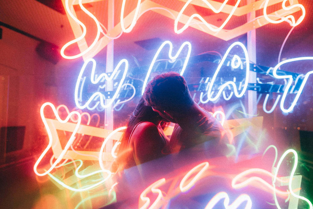 a young couple kissing in front of a neon light wall