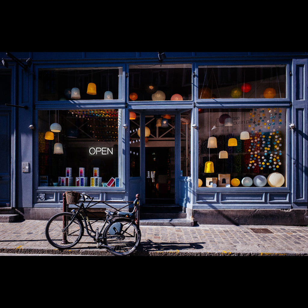 a lighting white open neon sign hanging on a blue store window